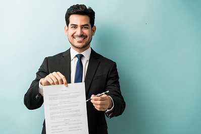 Portrait of smiling confident young male professional with contract against colored background